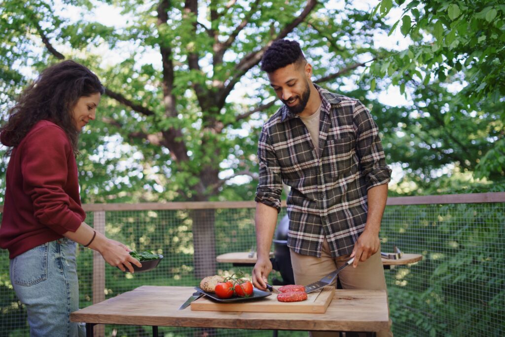 Couple preparing burgers outdoors in a tree house, weekend away and digital detox concept.