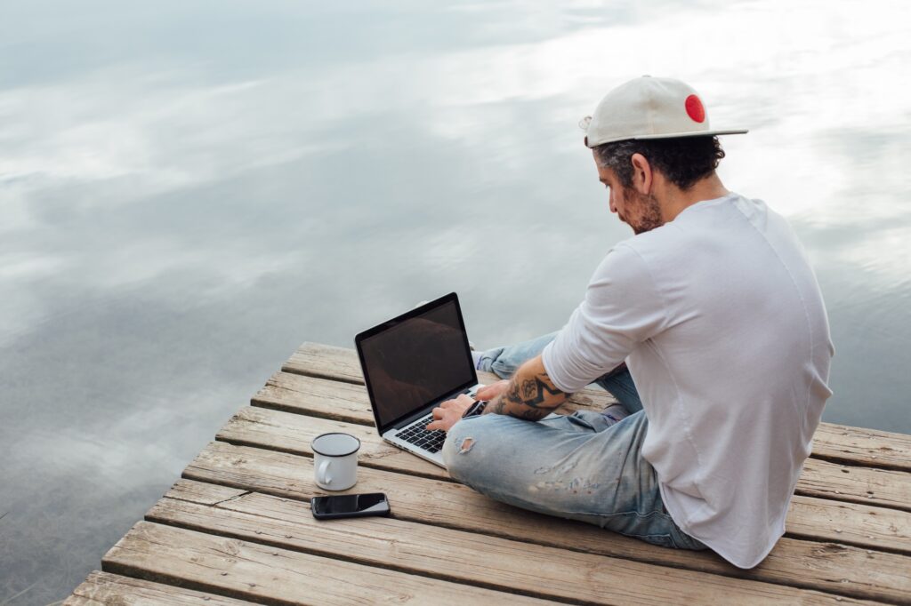 Man works on laptop at pier on lake or sea