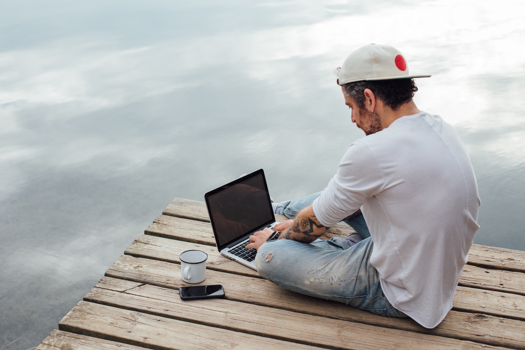 Man works on laptop at pier on lake or sea